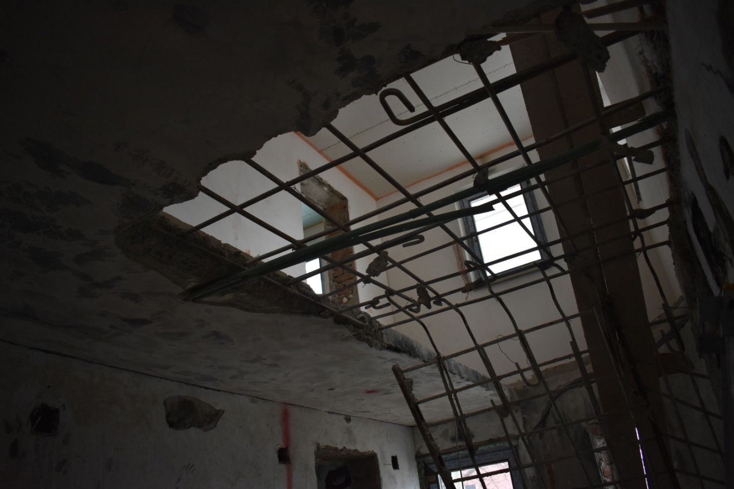 Vedere de jos spre o placă de beton armat spartă, cu plasă de armătură expusă