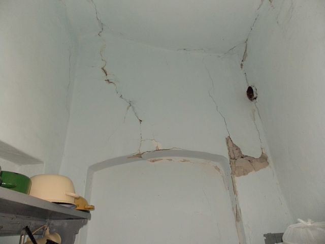 Colț de încăpere cu mai multe fisuri ramificate și tencuială desprinsă.